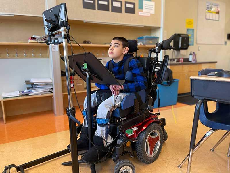 A student working on his communication device that is mounted on his wheelchair