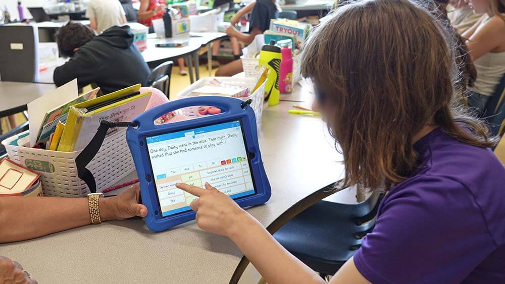 In a classroom, a student is pointing at a tablet with Clicker app