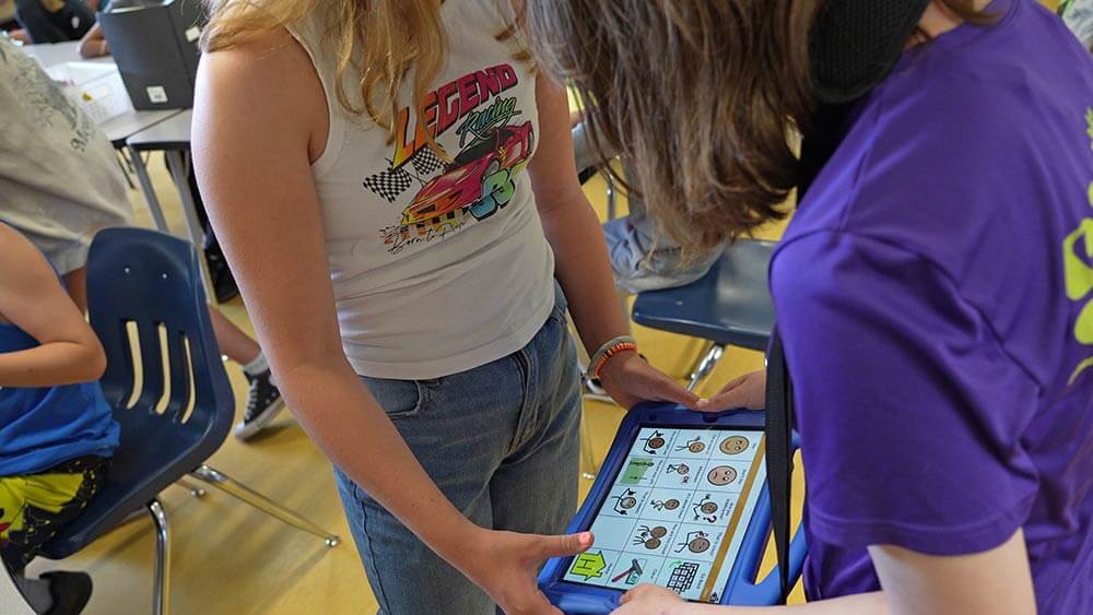 Two students in the classroom looking at an iPad with TouchChat software